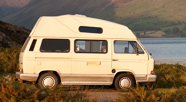 Autocaravana blanca frente a un lago en medio del campo