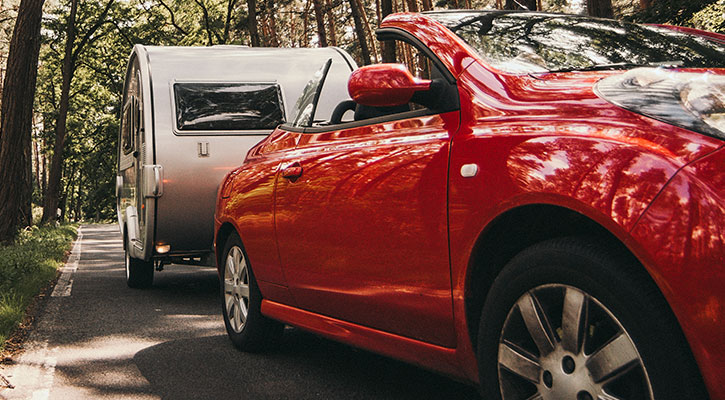 Descapotable rojo con una caravana blanca que circula por una carretera rural
