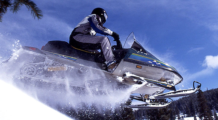 Alguien volando sobre una colina en su moto de nieve, cielo azul de fondo