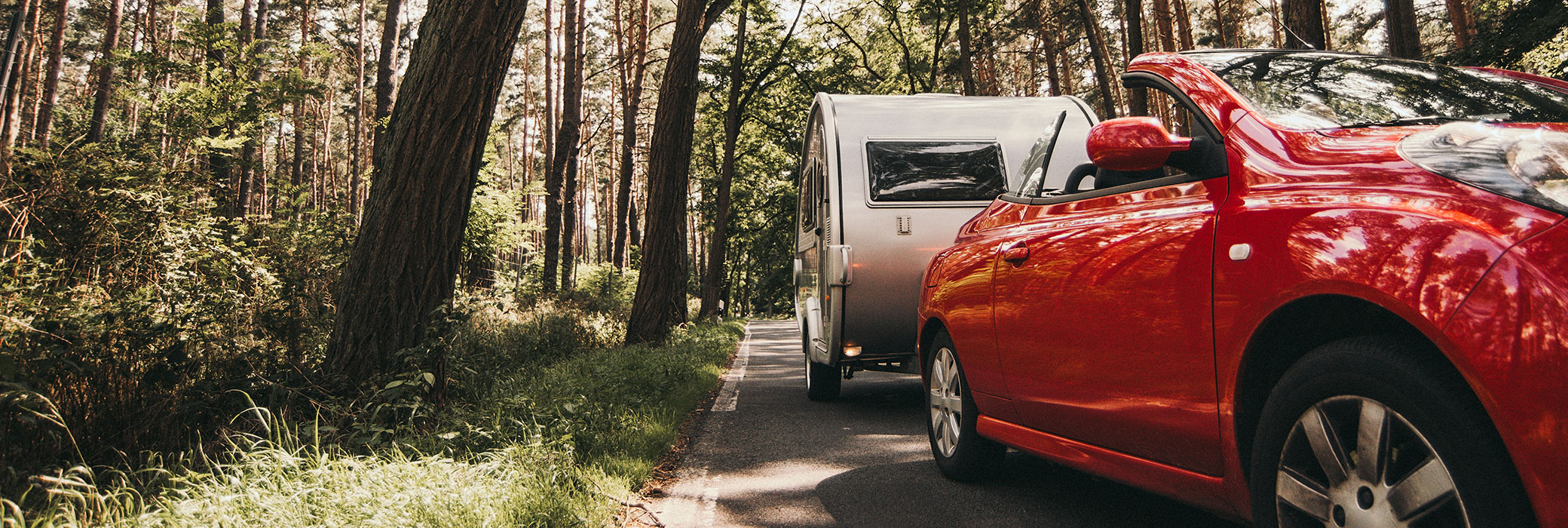 Red cabriolet with a white caravan driving down a country road