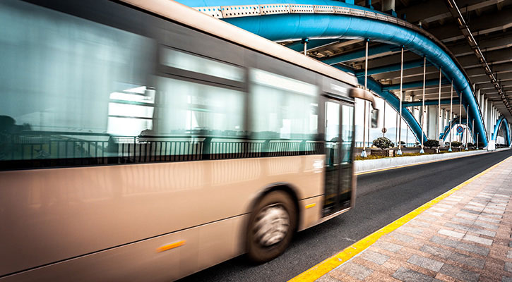 Autobús blanco cruzando un puente con arcos metálicos de color azul y blanco